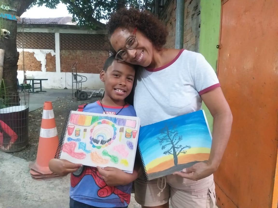 Educadora e aluno mostrando desenhos feitos em oficina do Espaço Cultural Márcio Conde